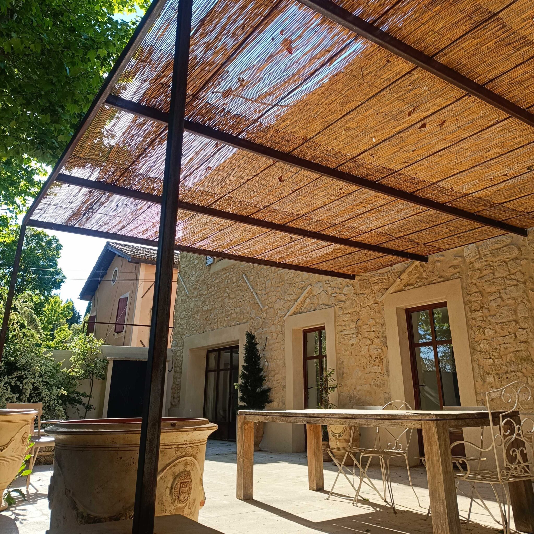 Pergola en fer avec toiture en canisses – structure artisanale posée contre une maison en pierre