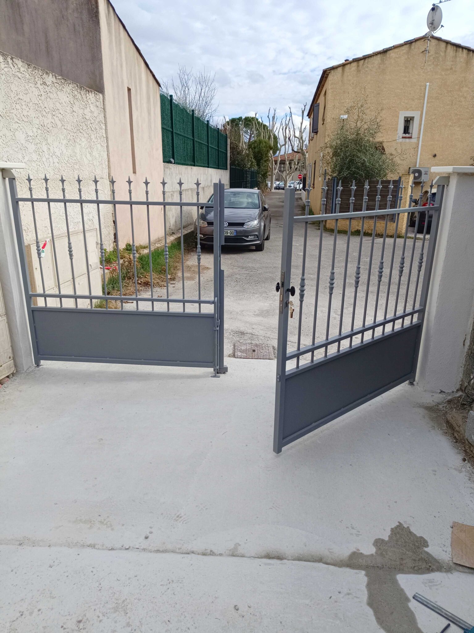 Portail ajouré en acier gris avec deux vantaux ouverts – vue depuis l’intérieur