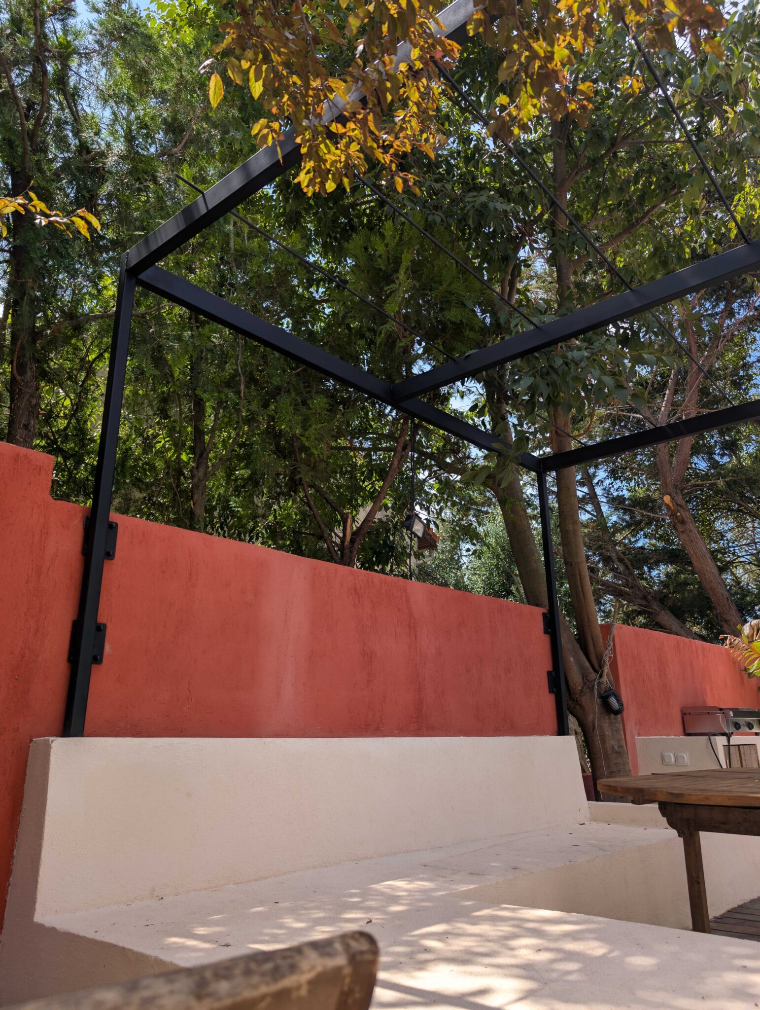 Vue rapprochée de la pergola en acier noir mat intégrée à un mur rouge, prête à accueillir des canisses.