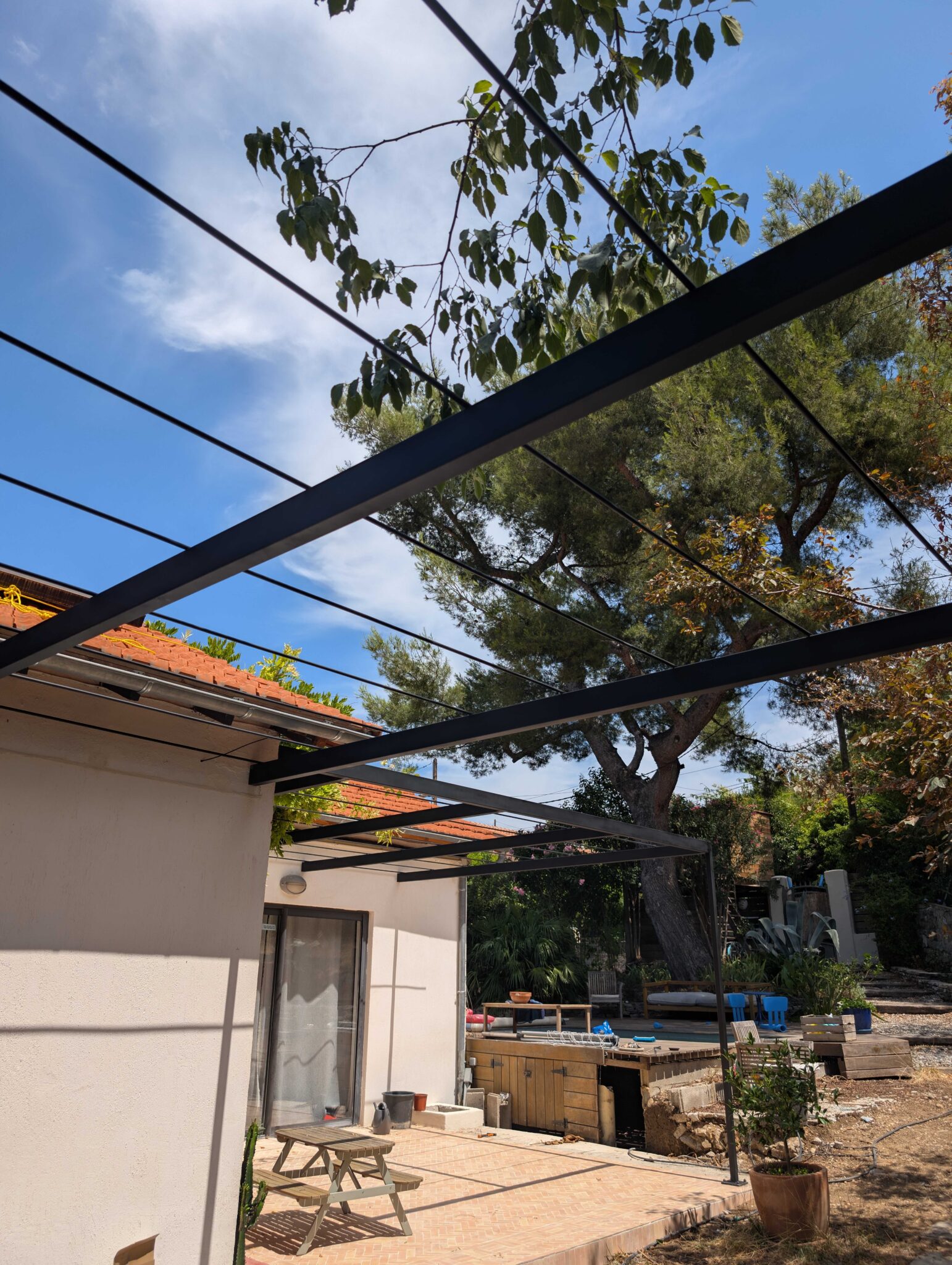 Structure en acier noir mat tendue entre deux murs, avec vue sur la cour et les arbres environnants.