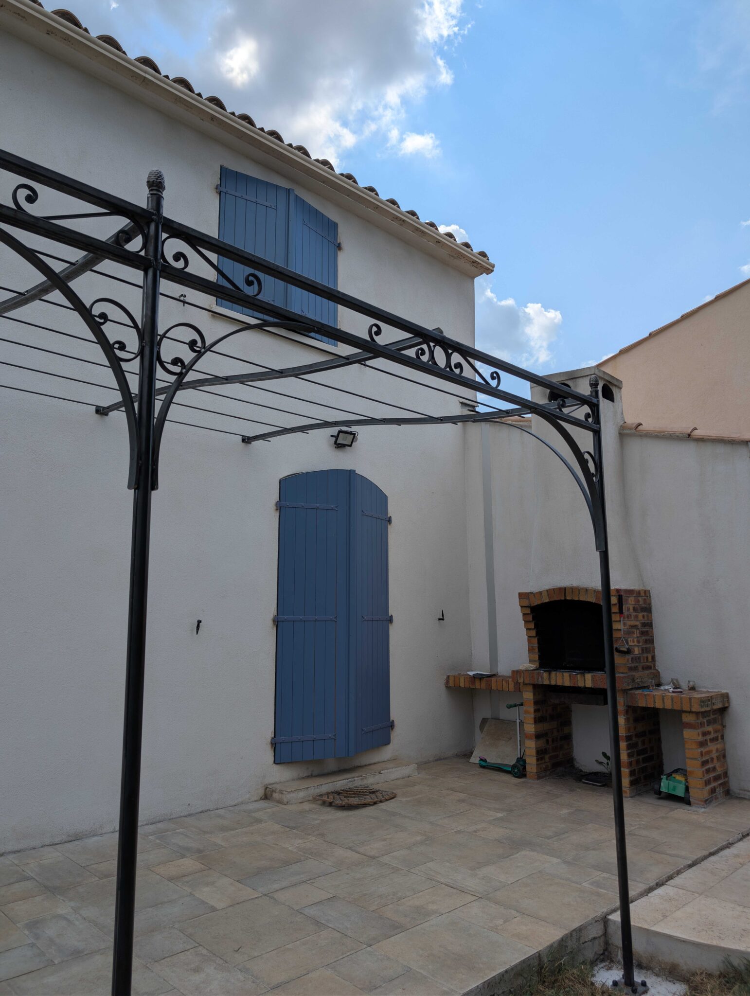 Pergola en fer forgé sur mesure en acier brut avec poteaux ronds, traverses en T et chapeau de gendarme.